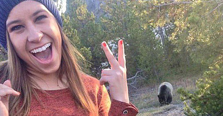 Jeune femme en train de prendre une photo avec un ours derrière 