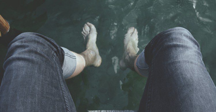 Personne ayant les pieds dans l'eau avec un poisson au fond de l'eau