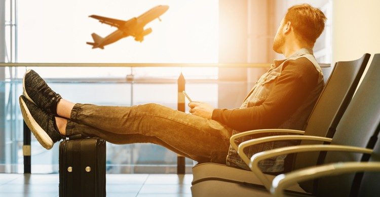 Homme assis dans un hall d'aéroport les pieds posés sur sa valise